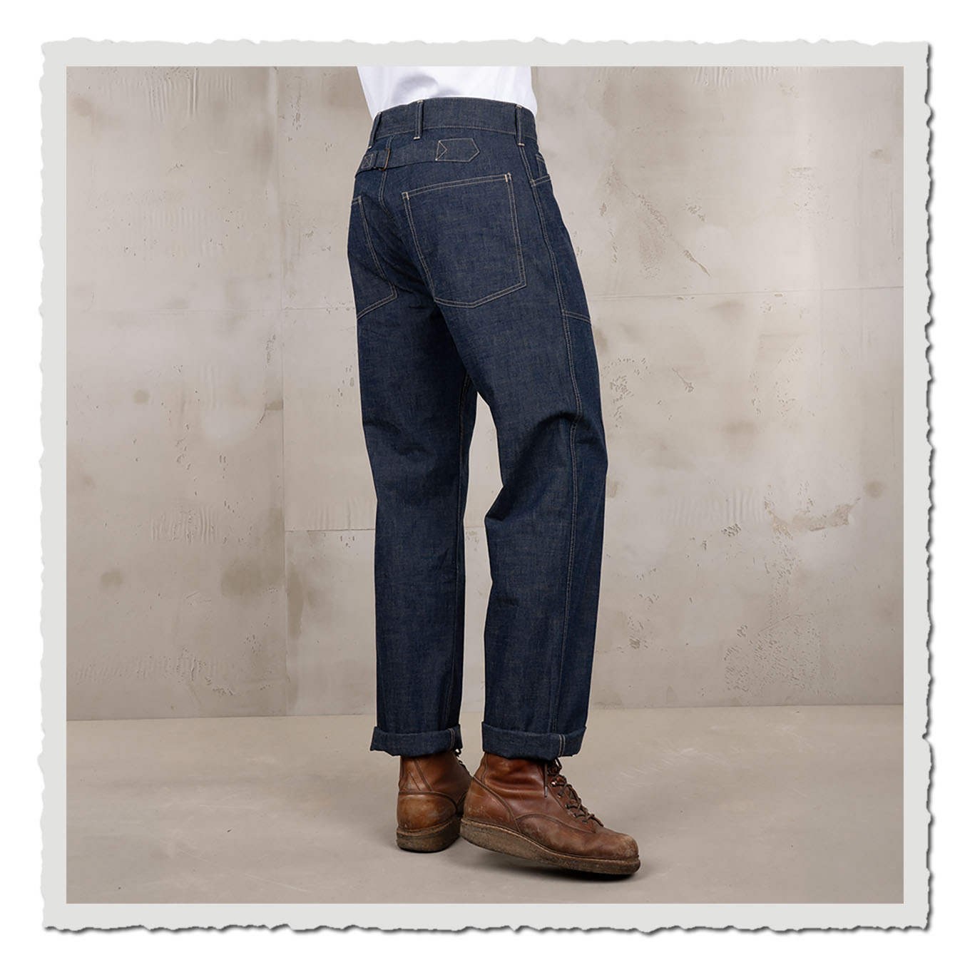 Indigoblaue Hose schräg von hinten getragen, kombiniert mit braunen Boots im Studio.